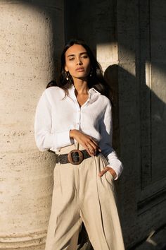 a woman in white shirt and tan pants leaning against column