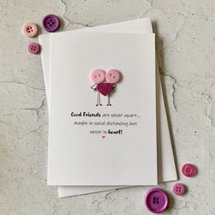 a card with two pink buttons attached to it on top of a white surface next to some purple buttons