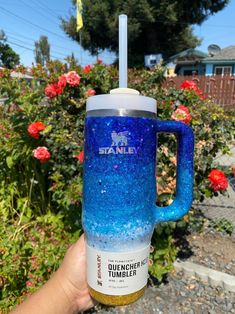 someone is holding up a blue and gold glittered coffee mug in front of some flowers