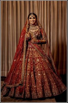 a woman in a red and gold bridal gown posing for the camera with her hands on her hips