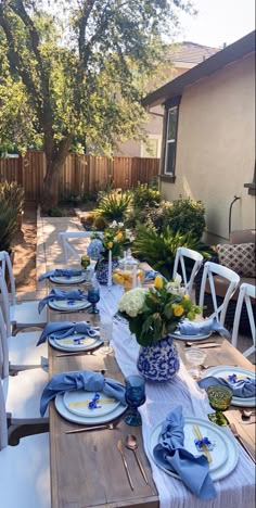 an outdoor table set with blue and white plates, place settings and flowers on it