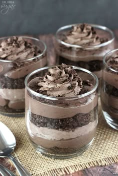 four desserts with chocolate frosting and oreo cookies in glass cups on a table