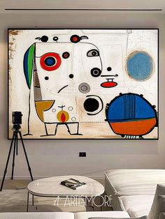 an abstract painting hangs on the wall above a white couch and coffee table in a living room