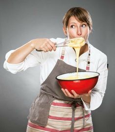 a woman in an apron is holding a red bowl and spoon with cheese being poured into it