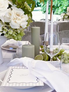 the table is set with white flowers and green fruit in vases next to candles