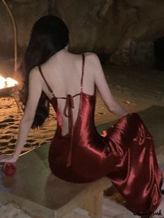 a woman in a red dress sitting on a rock next to the ocean at night