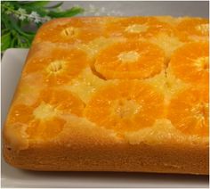 an orange cake on a white plate with flowers in the backgroung area