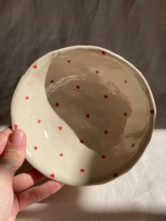 a hand holding a white bowl with red hearts on it