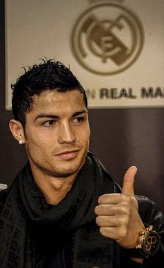 a man giving the thumbs up sign in front of a wall that reads real madrid