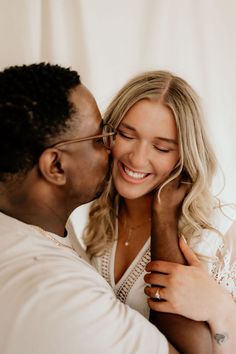 a man kissing a woman's forehead in front of a white curtain