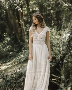 a woman standing in the woods wearing a white dress