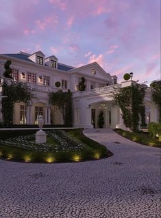 a large white house with lots of windows and plants on the front lawn at dusk