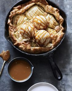 an apple pie in a cast iron skillet with caramel sauce and spoon on the side