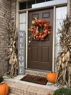 a welcome sign is displayed on the front door of a house with pumpkins and corn stalks