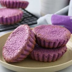 three purple cookies on a plate next to a cooling rack