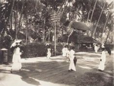 an old black and white photo of people walking on a boardwalk in front of palm trees