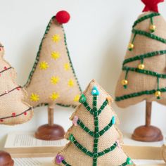 three burlap christmas trees sitting on top of a wooden table next to an open book