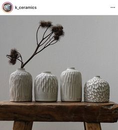 three white vases sitting on top of a wooden table next to a plant in a vase