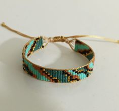 a close up of a beaded bracelet on a white surface with a gold string