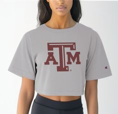 Elevate your Aggie game day attire with our Women's Texas A&M Logo Crop Top, a timeless piece that exudes pride and tradition. Crafted from premium 100% cotton, this tee ensures superior comfort during those intense moments cheering on the Aggies at Reed Arena or exploring the scenic beauty of Aggieland. Featuring the iconic Texas A&M logo front and center, this crop top is a true testament to your Aggie spirit. Whether you're attending class or hitting up Northgate for post-game celebrations, t University Logo Short Sleeve Top For Sports Season, Collegiate Tops With University Logo For Game Day, Fitted T-shirt With Team Name For Game Day, Collegiate Athletic Heather Tops For Sports Events, Athleisure Cotton T-shirt With Team Name, University Logo Short Sleeve Tops For Fans, Sports Tops With University Logo For Sports Season, University Logo Sports Tops For Sports Season, Athleisure Crew Neck Top For Fan Gear