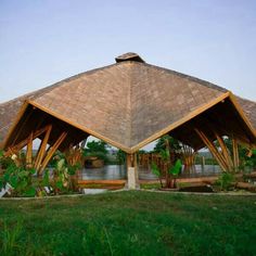 an open air pavilion with grass roof and water in the backgrouds, surrounded by greenery