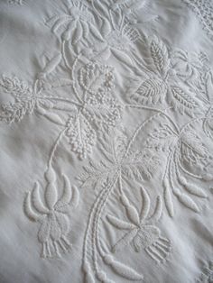 an embroidered tablecloth with white threadwork and flowers in the center, on a wooden surface