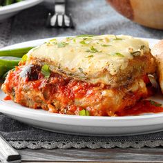 a white plate topped with lasagna covered in sauce and cheese next to green beans