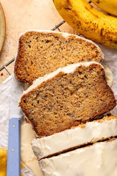 two slices of banana bread with icing on a cutting board next to some bananas