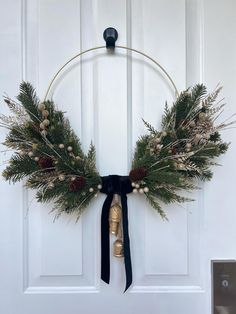 a wreath on the front door with bells and greenery hanging from it's side