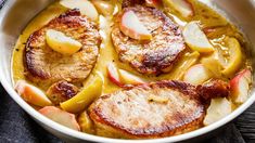 a pan filled with meat covered in gravy and apple slices on top of a table