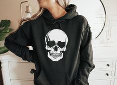 This fun Halloween Skull Hoodie on a unisex hoodie is great for Halloween and the fall season! More colors available in the shop under the Halloween Tab. For other products or premium hoodies, message me. For an oversize fit, size up 1-2 bigger. UNISEX Heavy Blend Hoodie | Gildan 18500 ⚡ 50% pre-shrunk cotton, 50% polyester ⚡ Air-jet spun yarn with a soft feel and reduced pilling ⚡ Double-lined hood with matching drawcord ⚡Front pouch pocket ARTWORK: Printed with (DTG) Direct to Garment printing Halloween Punk Hoodie With Skull Print, Punk Halloween Hoodie With Skull Print, Punk Halloween Hoodie With Skull Design, Punk Skull Hoodie For Halloween, Halloween Skull Print Sweatshirt For Streetwear, Halloween Skull Sweatshirt In Black, Halloween Punk Hoodie Tops, Black Skull Sweatshirt For Halloween, Punk Halloween Hoodie Top