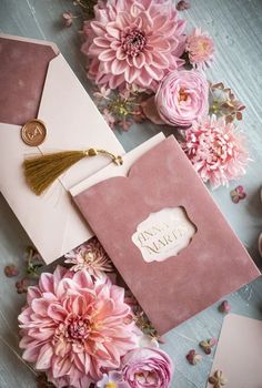 pink flowers and white envelopes with gold tasseling on the inside are scattered around