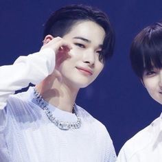 two young men standing next to each other in front of a blue background and wearing white shirts