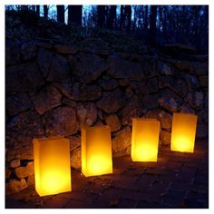 four glowing paper lanterns sitting on the ground in front of a stone wall at night