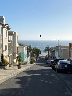 cars parked on the side of a street next to some buildings and ocean in the background