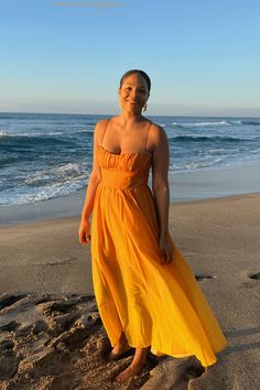 a woman in an orange dress standing on the beach