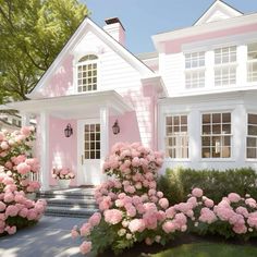 a pink house with white trim and lots of flowers on the front lawn in front of it