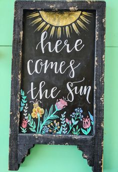 there is a chalkboard sign with the words here comes the sun written on it