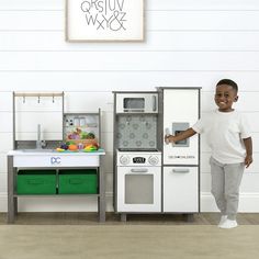 a young boy standing in front of a play kitchen