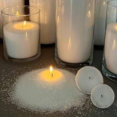 some candles are sitting on a table next to other glass vases and containers with white stuff in them