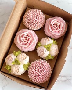 four cupcakes in a box with pink frosting and flowers on the top