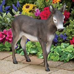 a toy donkey standing in front of colorful flowers and greenery on a brick walkway