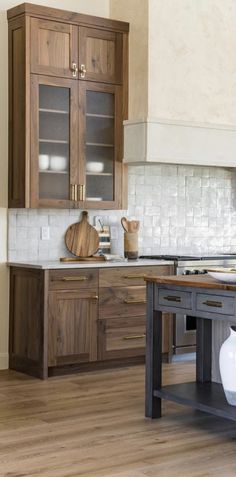 a kitchen with wooden cabinets and white tile backsplash, wood flooring and an island in the middle