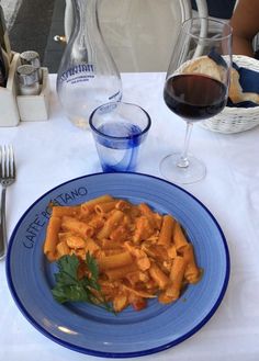 a blue plate topped with pasta next to a glass of wine