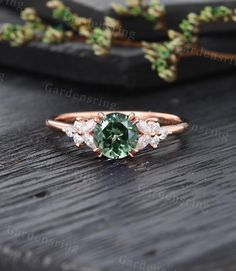 an oval green and white diamond ring sitting on top of a wooden table next to flowers