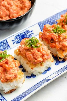 four pieces of sushi on a blue and white platter with a bowl of sauce in the background