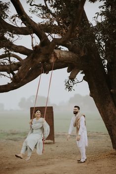 a man and woman standing next to each other on a swing in the middle of a field