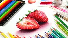 two strawberries are sitting next to colored crayons and pencils on the table