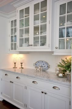 a kitchen with white cupboards and marble counter tops, along with silver candlestick holders