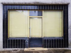 an empty store front with yellow shutters on the doors and window sill behind it